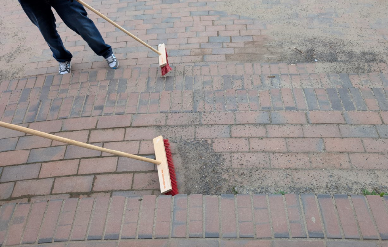 Kinder fegen den Schulhof beim Frühjahrsputz